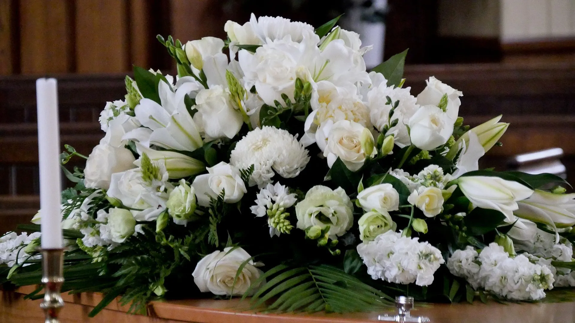 A serene arrangement of white lilies, roses and carnations resting beside a candle in the Hardwick & Sons chapel