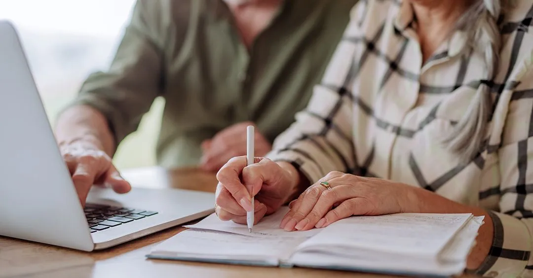 An older couple sitting together with a notebook and laptop, planning arrangements in advance